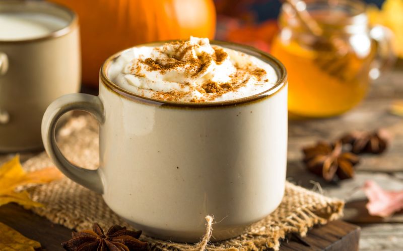 A latte in a clear mug with a cinnamon stick garnish, and a drizzle of honey.